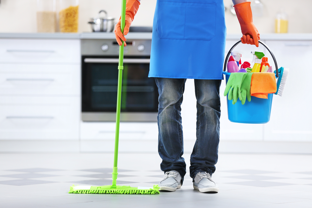 a uniformed cleaner with a mop and cleaning materials, cleaning a kitchen