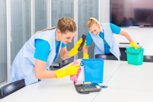 two uniformed cleaning staff working on a table surface