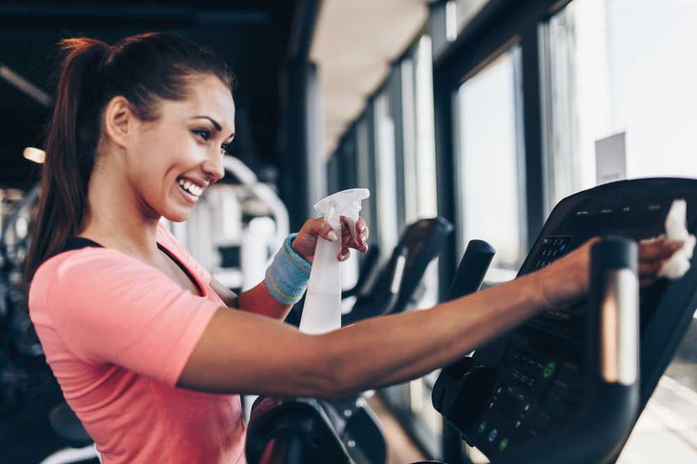 a smiling woman cleans a gym machine 