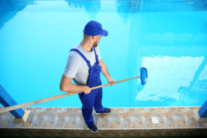 a uniformed cleaner uses a tool to clean a swimming pool