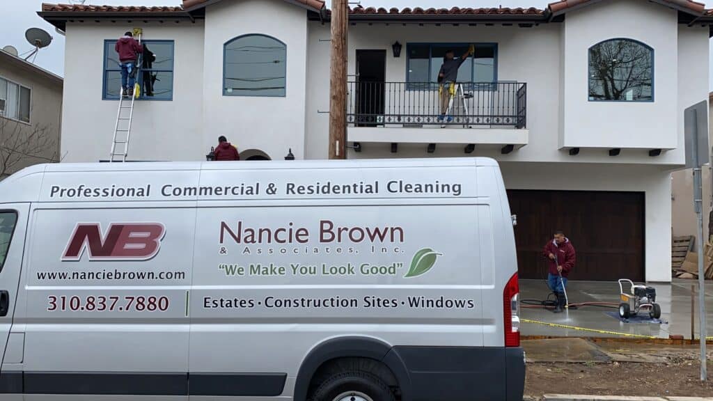 Nancie Brown & Associates van parked in front of a residential property as crew members perform post-construction cleaning, including window and exterior detailing.