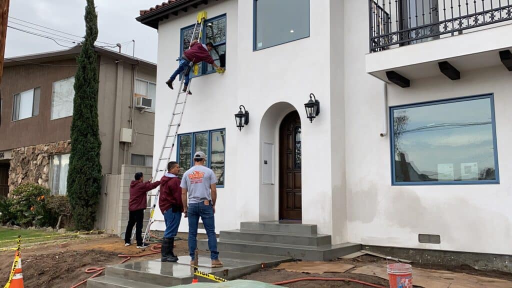 Nancie Brown & Associates team performing exterior window cleaning on a residential property during a post-construction cleanup, using ladders and safety equipment.